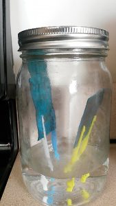 A picture of a jar which includes pieces of copper (now coated with verdigris) suspended in a layer of vinegar.