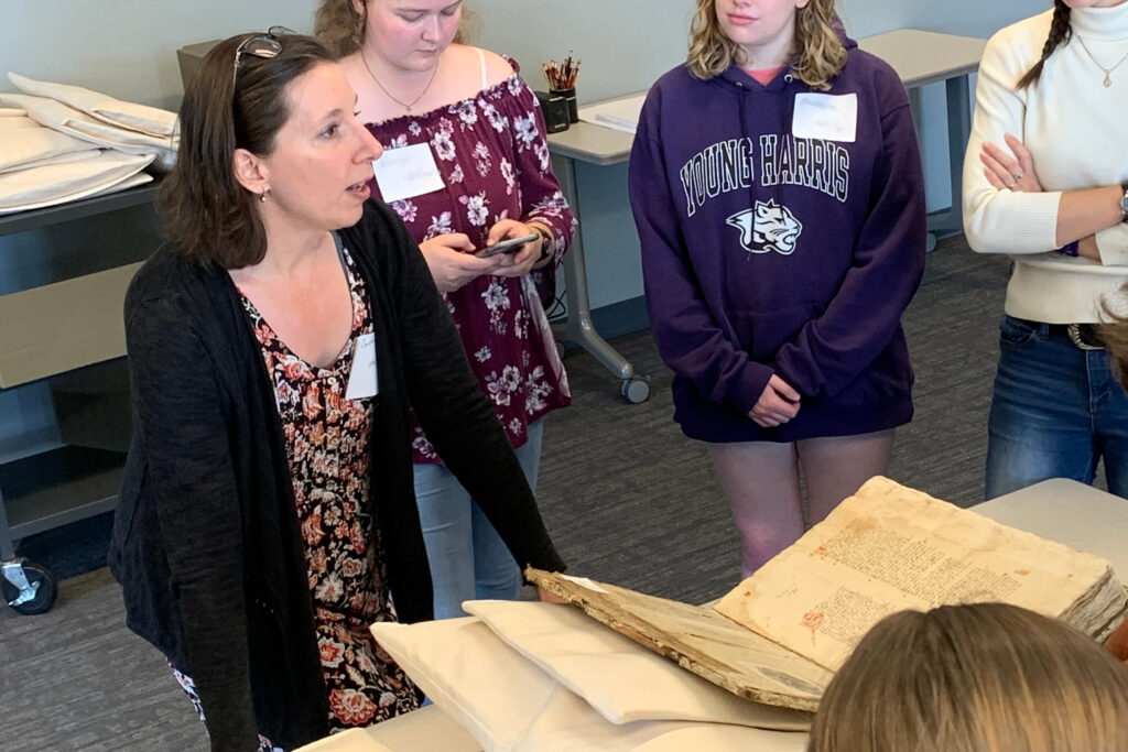 A professor and some students stand around an open medieval manuscript
