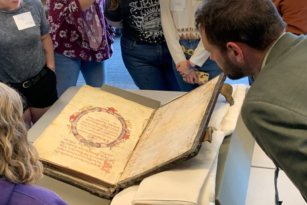 A professor and students look closely at an open medieval book.