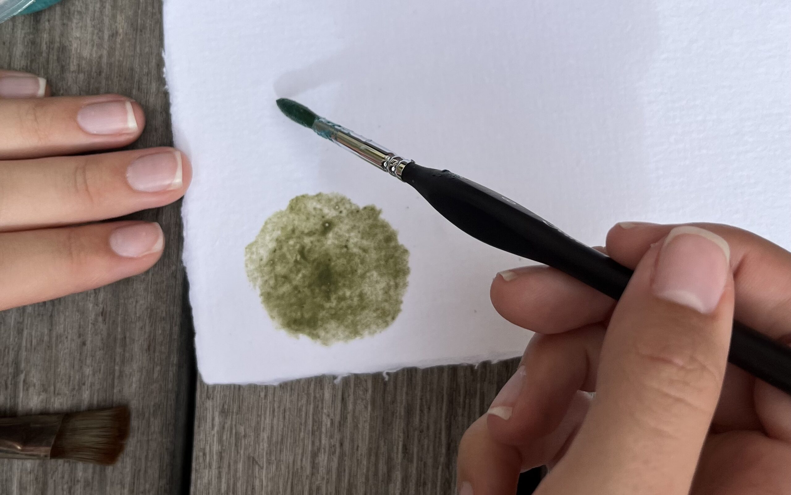 Student holding brush, painting a circle of green earth on paper