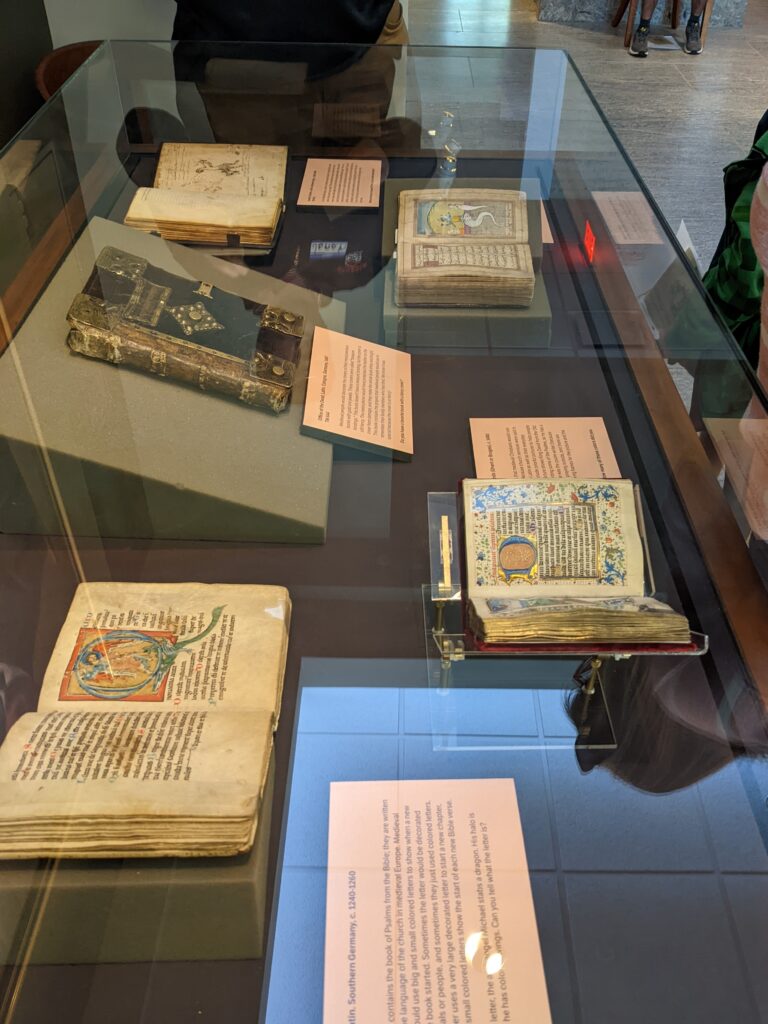 open and closed medieval manuscripts, with caption labels, in a museum display case