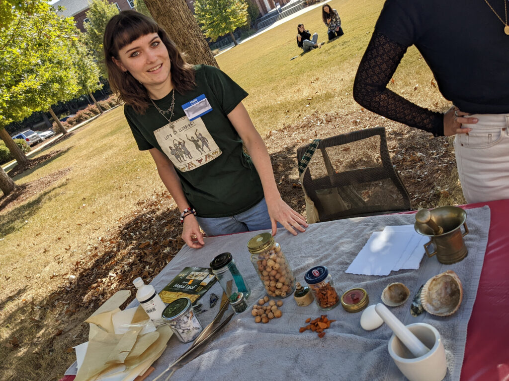two students stand in front of a table outside. on the table sits an array of natural materials and implements.