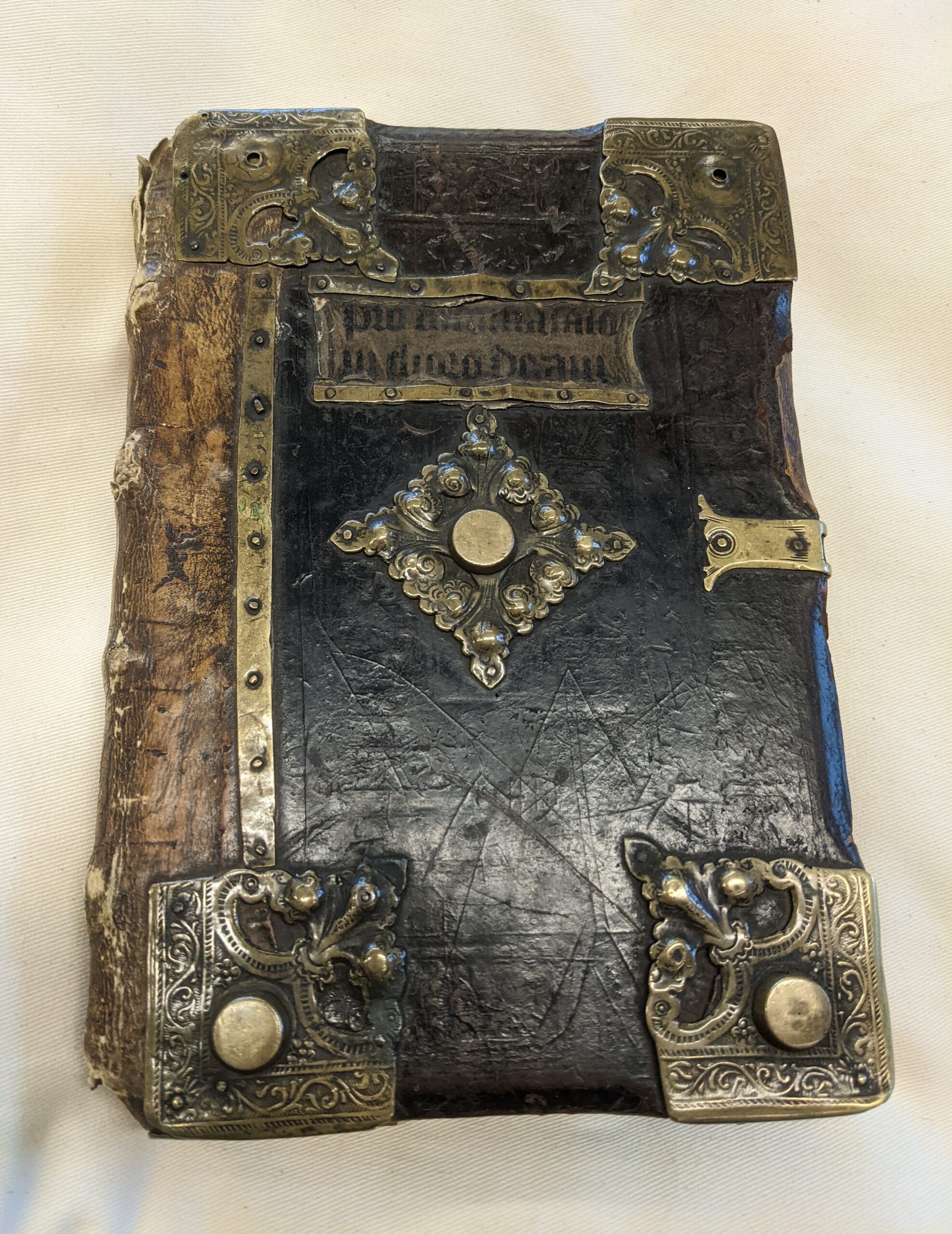 An old book with a wooden and leather cover, with metal pieces on the corners, in the center, and with a clasp