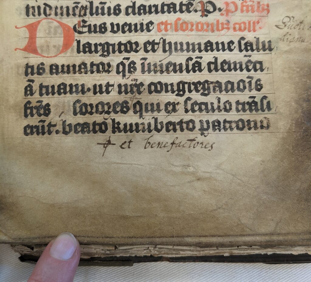 Part of a worn parchment page written in red and black gothic script. Words in a different hand are added in the lower and side margins. 