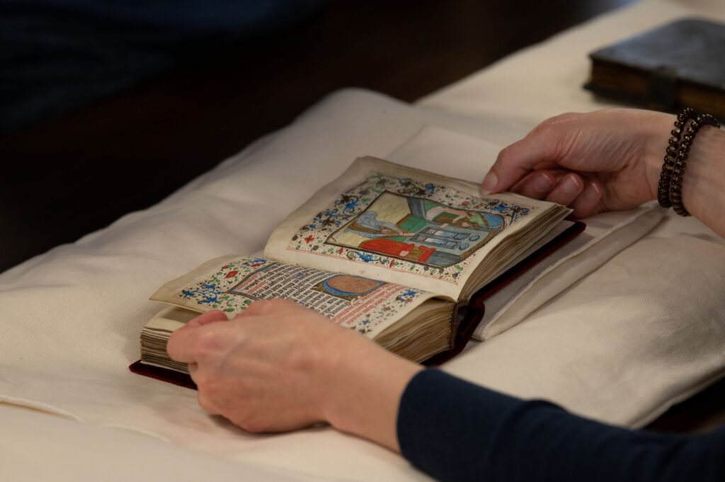 Two hands hold open a medieval book with colorful miniatures and decorations.