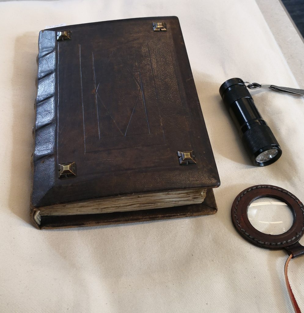 A photograph of the manuscript sitting on a support pillow with the UV flashlight and a magnifying glass next to it.